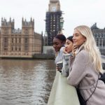 Three women gaze at the Big Ben clock tower in London, capturing the moment in front of the famous landmark